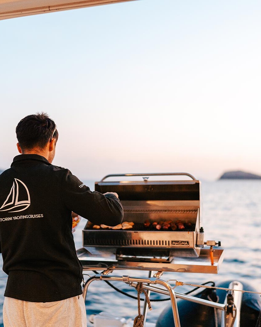 Crew cooking a BBQ on a Catamaran whilst sailing in Santorini