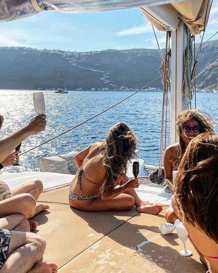 Friends having fun on the deck of a catamaran sailing through the caldera in Santorini