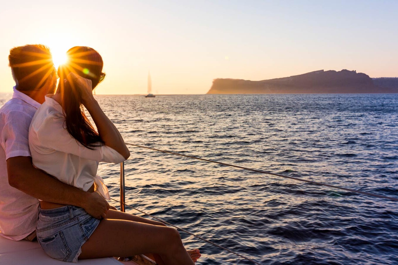 Couple sitting on catamaran sailing in to the sunset in the caldera Santorini